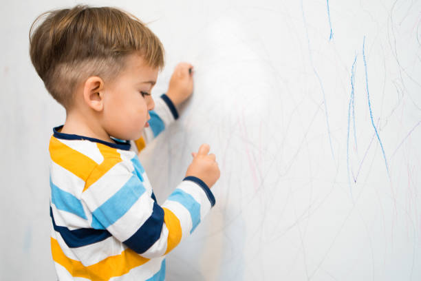 niño escribiendo en la pared blanca de su habitación con crayones