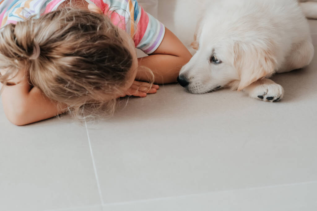 niña cachorro mascota perro Golden Retriever yacen juntos en el piso copia espacio amistad blanco beige natural colores pastel baldosas de porcelana.